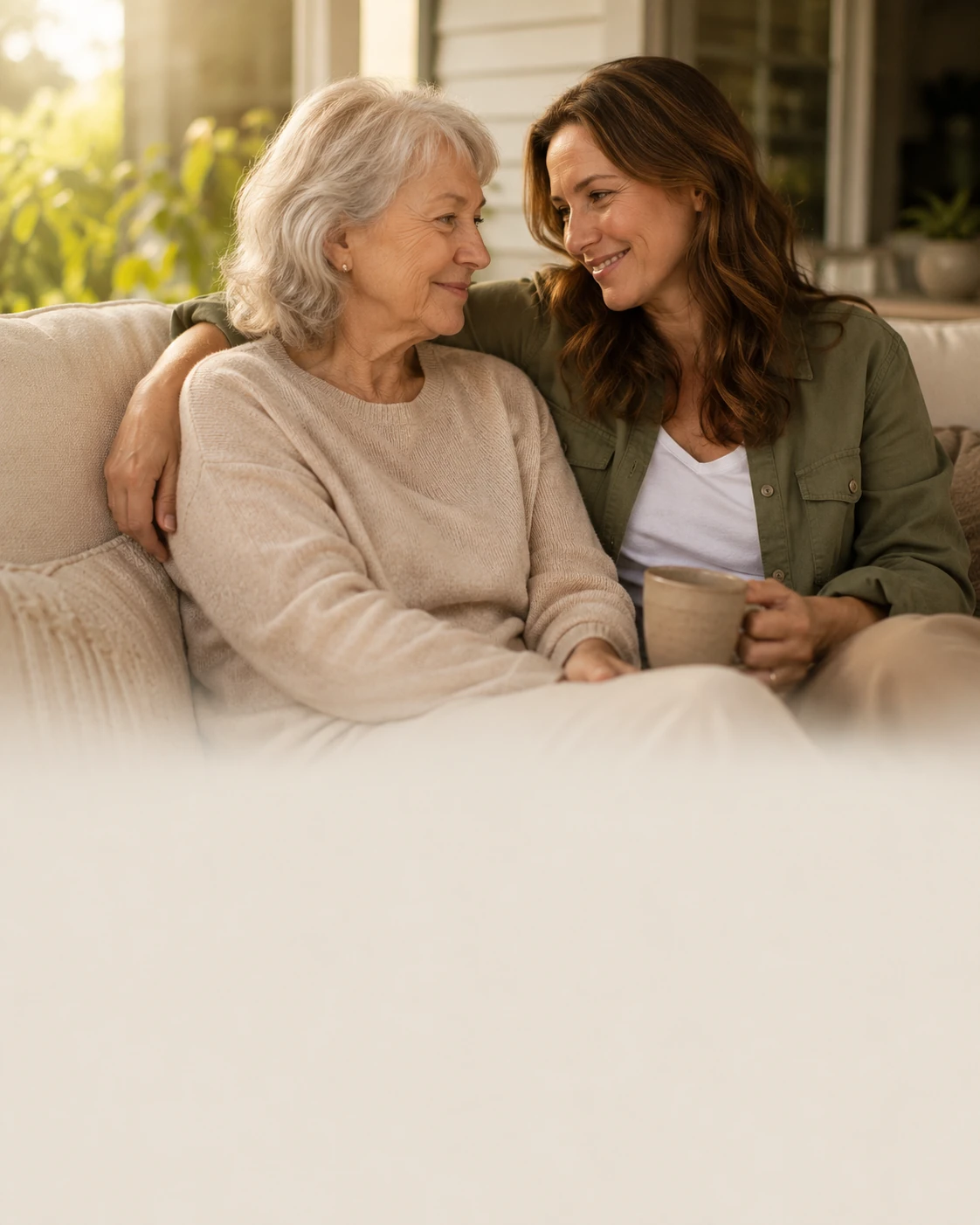 An older woman and her adult daughter sitting close together at home, smiling